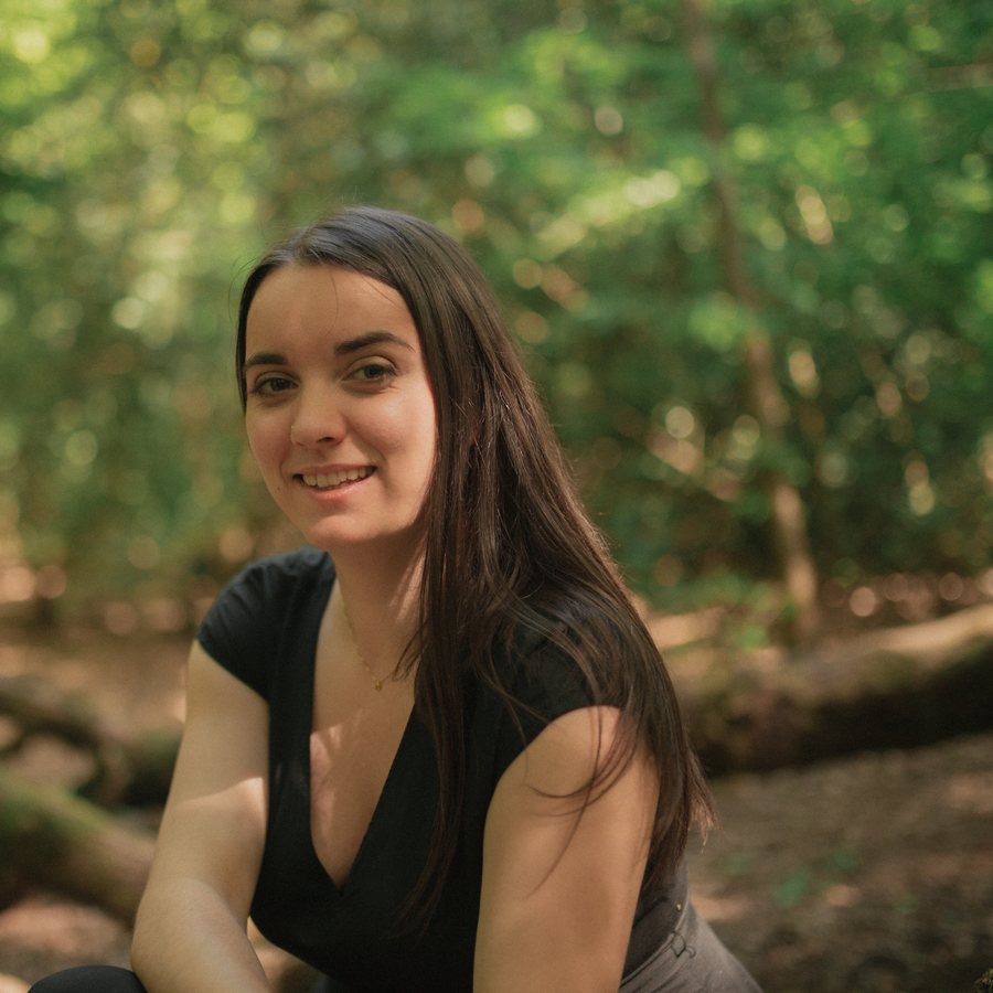 Lilli Unwin sitting in a sunlit wood, smiling.