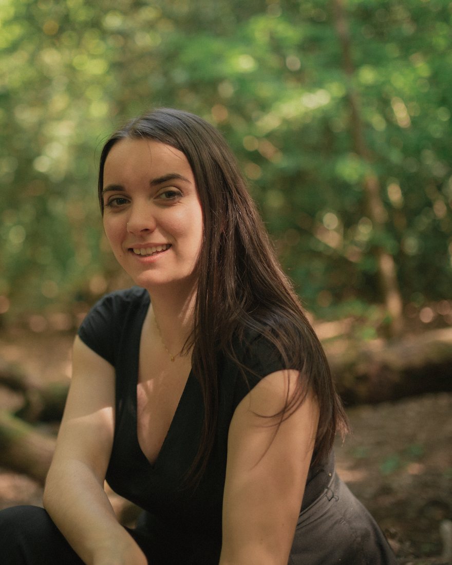 Lilli Unwin sitting in a sunlit wood, smiling.